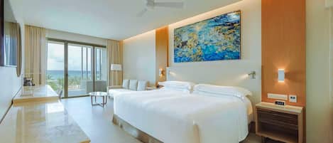 Una habitación de hotel moderna con una cama grande, un escritorio, un televisor de pantalla plana, un ventilador de techo, un cuadro y vista al océano.