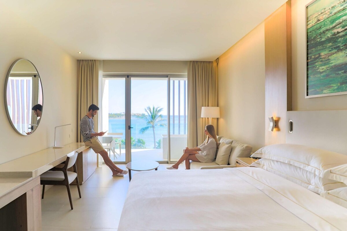 A hotel room with a large bed, a desk, a chair, and a view of the ocean.