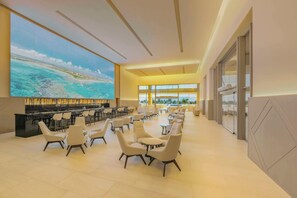 Un vestíbulo amplio con una pantalla grande que muestra una escena de playa, asientos cómodos y una zona de bar moderna.