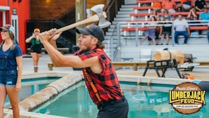Una persona sostiene un hacha grande cerca de una piscina, con espectadores de fondo.