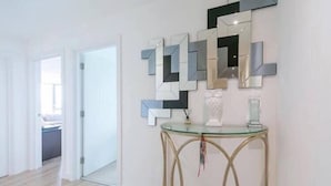 A modern interior with a glass console table, geometric wall mirrors, and a visible doorway leading to another room. - Stylish 1 Bedroom Apartment near London City (London)