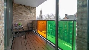 A balcony with a brick wall, a table with chairs, and a view of buildings through a glass partition. - Stylish 1 Bedroom Apartment near London City (London)