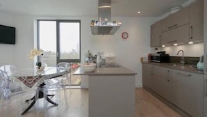 A modern kitchen with a central island, a dining area with a glass table, and a view of the city through large windows. - Stylish 1 Bedroom Apartment near London City (London)