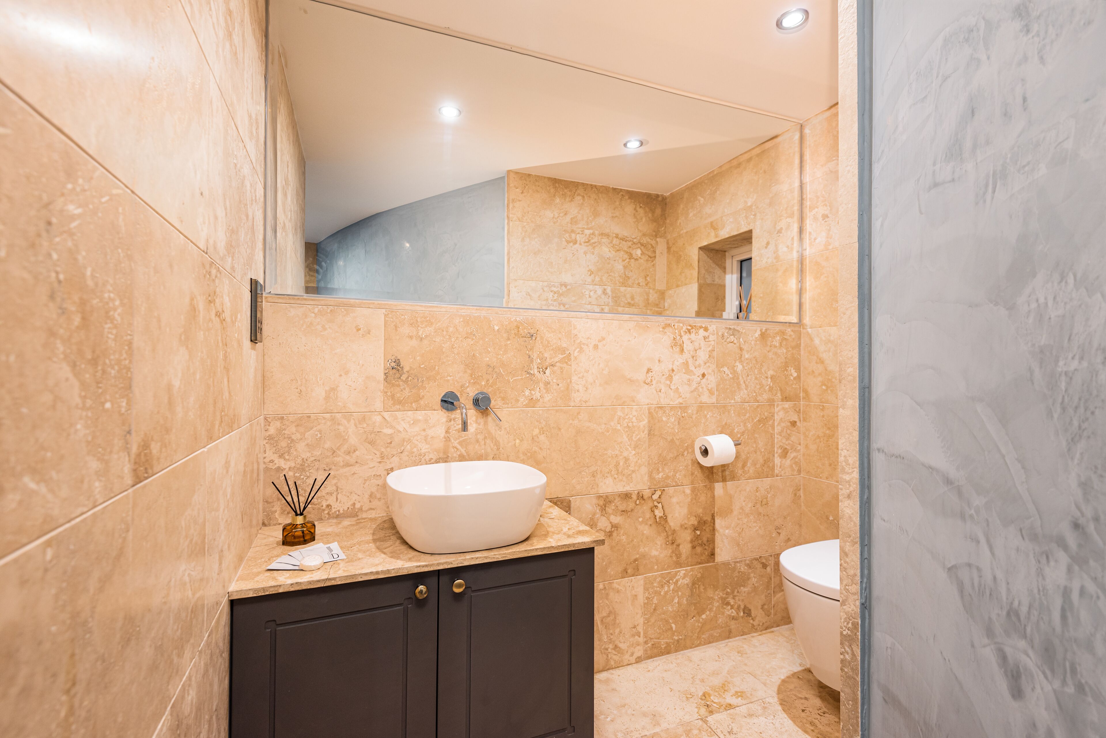 A modern bathroom with a large mirror, a vessel sink, dark cabinets, and a toilet.