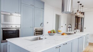 Een moderne keuken met lichtblauwe kastjes, een wit marmeren aanrecht, roestvrijstalen apparatuur en een centraal eiland met een spoelbak en een fruitschaal.