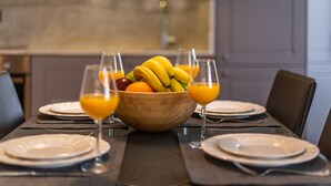 Een eettafel gedekt met borden, bestek, een fruitschaal en glazen jus d'orange.