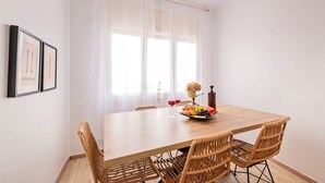 A dining area with a wooden table, wicker chairs, a fruit bowl, and two wine glasses. - Sweett | Rocafort 604 (Barcelona)