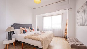 A bedroom with a bed, bedside table, lamp, and a window with a view. - Sweett | Rocafort 604 (Barcelona)