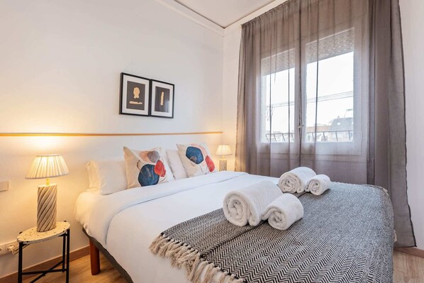 Une chambre d’hôtel avec un lit, deux lampes de chevet, une fenêtre avec des rideaux et deux tableaux encadrés accrochés au mur.