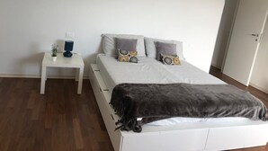 Un dormitorio con cama, mesita de noche, lámpara y una pequeña planta.