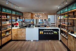 A modern cafe interior with wooden shelves, a coffee bar, and a variety of beverages and snacks.