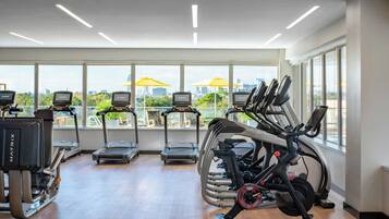 Un gimnasio moderno con cintas de correr, elípticas y bicicletas estáticas. Amplios ventanales ofrecen vistas panorámicas de la ciudad.