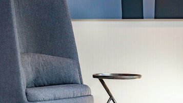 Una habitación moderna con un sillón tapizado gris, una mesita redonda con base de metal y un cuadro abstracto grande en la pared.