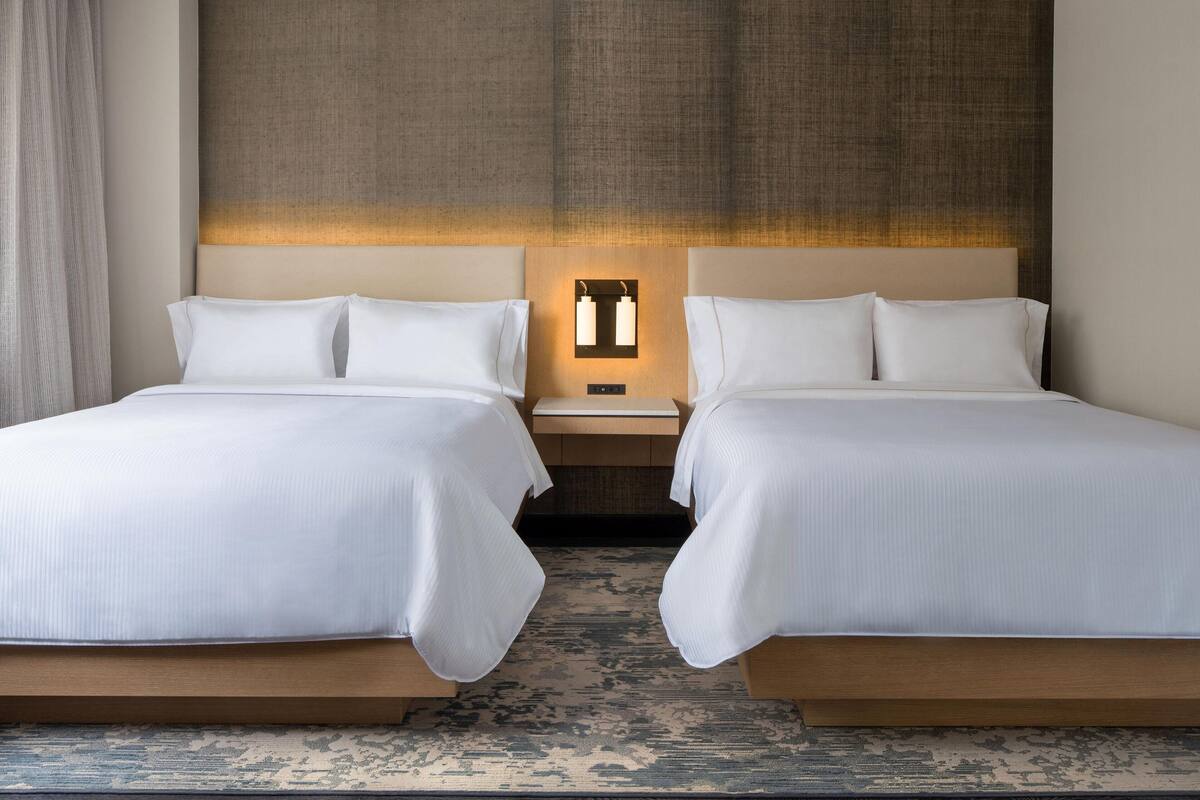 A double room with two beds, a nightstand, and a wall-mounted light fixture.