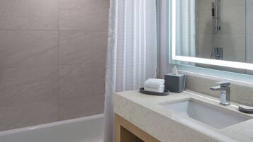 A modern bathroom with a bathtub, a large mirror, and a vanity with a sink and towel rack.