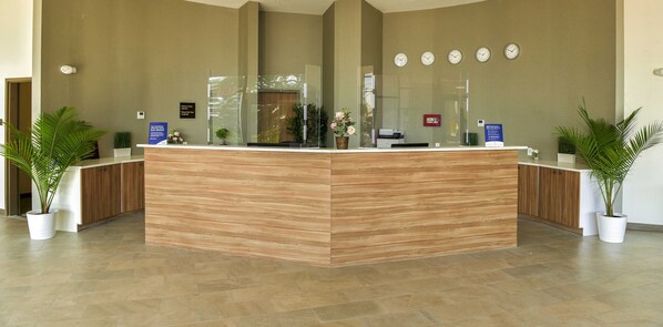 A reception desk with a wooden finish, a glass partition, and a clock on the wall.