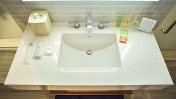 A bathroom sink with a white countertop, a soap dispenser, a hand soap dispenser, a toothbrush holder, and a sign with product information.