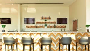 A modern bar area with a zigzag patterned wall, a long counter with multiple bottles, and four bar stools. - Wyndham Garden North Bergen Near Secaucus (North Bergen)