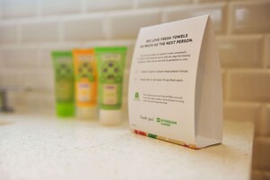 Un baño con encimera blanca, un cartel sobre toallas limpias y tres botellas de artículos de tocador.