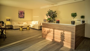 A modern living room with a sofa, two gold coffee tables, a wooden reception desk, and a potted plant. - Wyndham Garden North Bergen Near Secaucus (North Bergen)