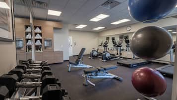 A gym with exercise equipment, a mirror, and a clock on the wall.