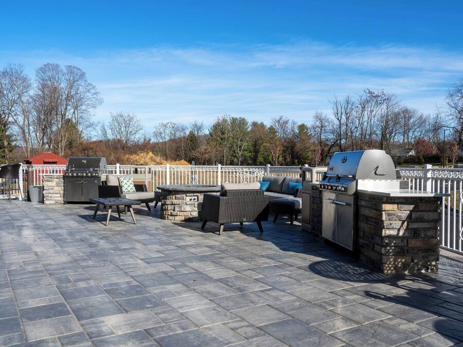 En udendørs terrasse med flisebelægning, grill og udendørs møbler.