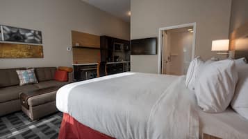 A hotel room with a large bed, a sofa, a kitchenette, and a TV.