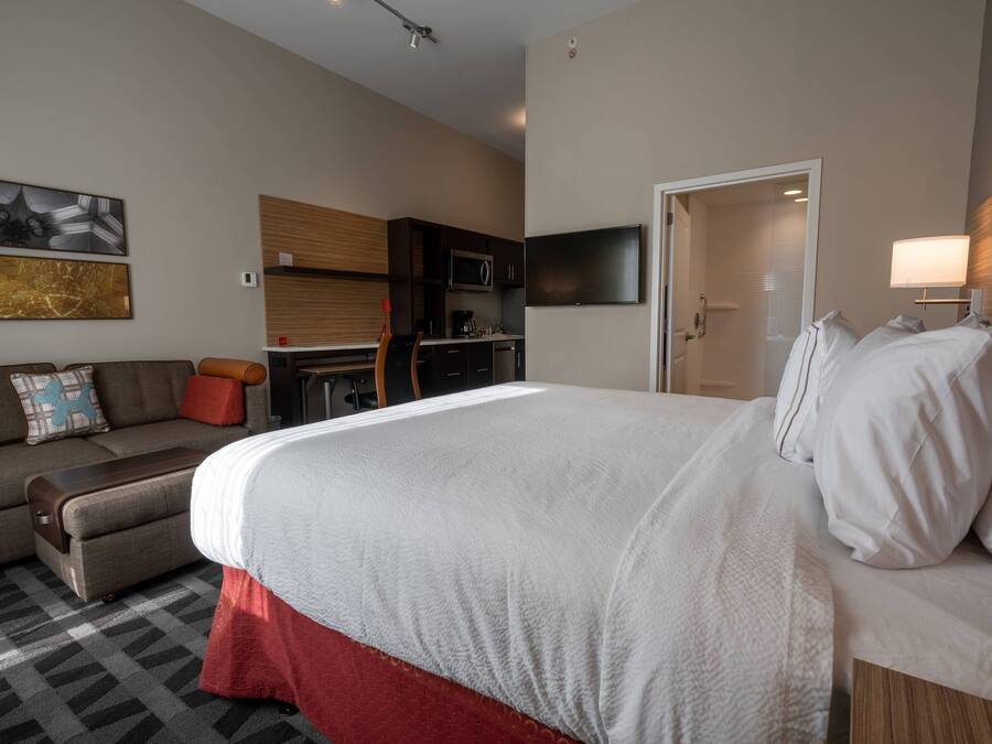 A hotel room with a large bed, a sofa, a kitchenette, and a TV.