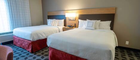A hotel room with two beds, a nightstand with a lamp, a chair, and a patterned carpet.