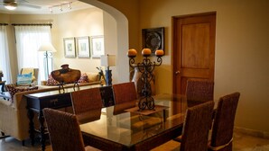 Un comedor con una mesa de vidrio y sillas de mimbre, una puerta de madera y una lámpara al fondo.