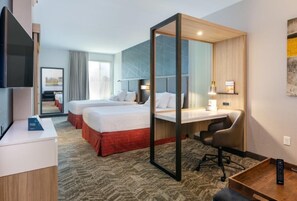 Habitación de hotel con dos camas, un escritorio, una silla, un televisor y un espejo grande.