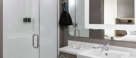 A modern bathroom with a glass shower enclosure, a white sink, and a large mirror.