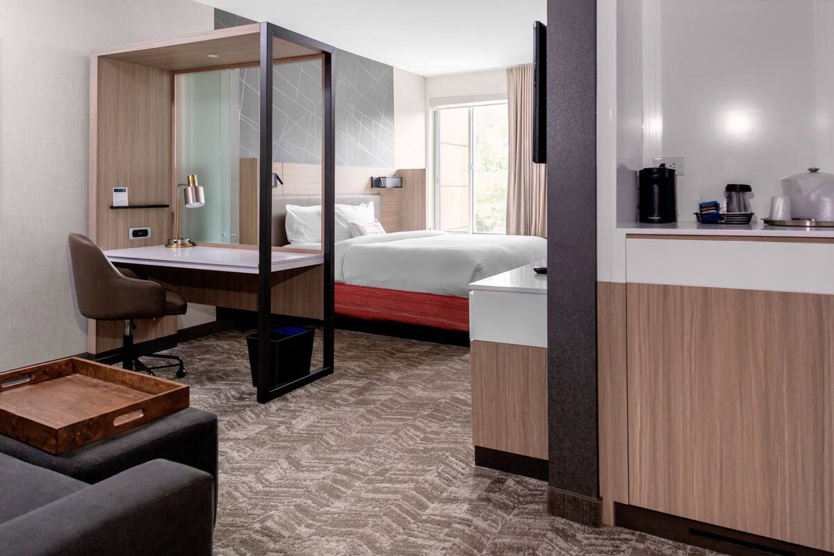 Habitación de hotel con cama, escritorio, silla y una pequeña zona de estar.