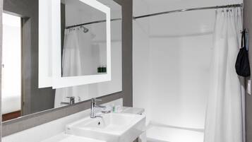 A modern bathroom with a large mirror, two sinks, a shower, and a bathtub.