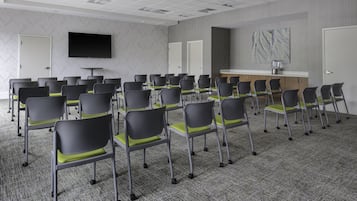 Una sala de conferencias con hileras de sillas, un televisor de pantalla plana, una estación de café y una puerta.