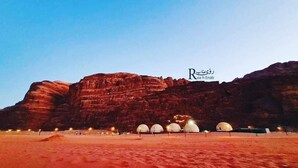 Un paysage désertique avec une grande formation rocheuse et plusieurs structures en forme de dôme, qui semblent être des logements, au premier plan.