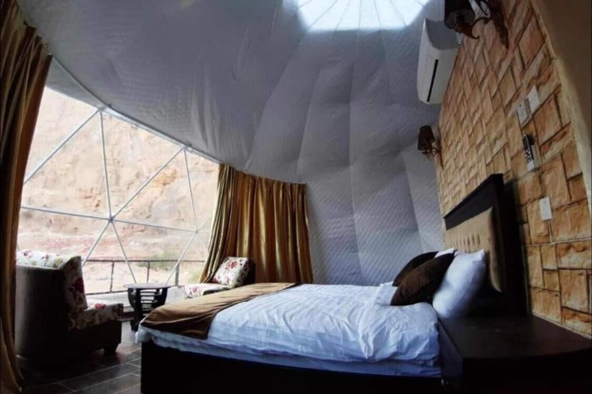 Una habitación con un ventanal grande, una cama, una silla y un muro con diseño de ladrillo.