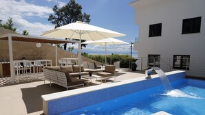 A swimming pool with a water feature, surrounded by outdoor seating and a pergola with umbrellas. - Modena Maris Apartments (Opatija)