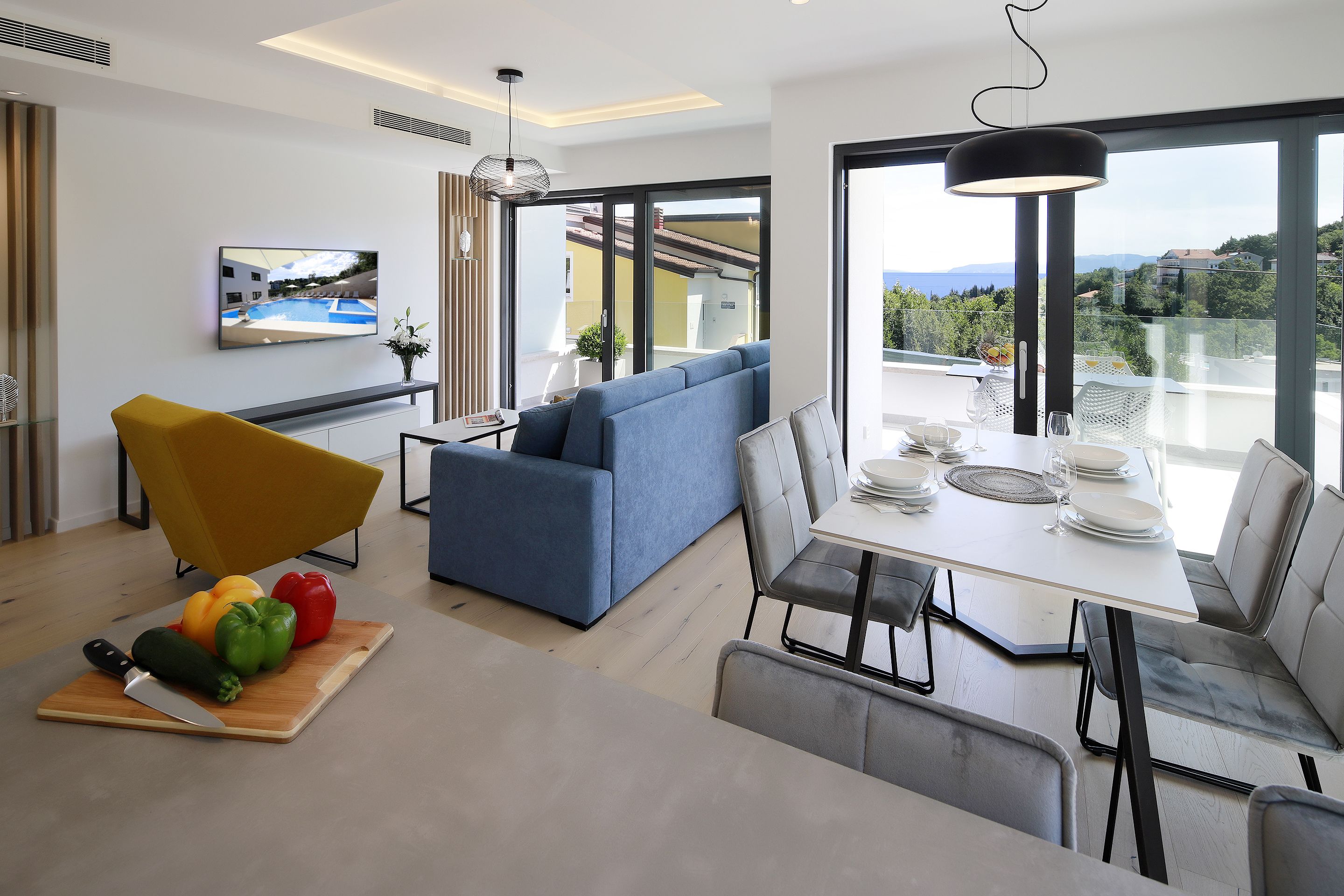 A modern living room with a sofa, dining table, and a TV mounted on the wall.