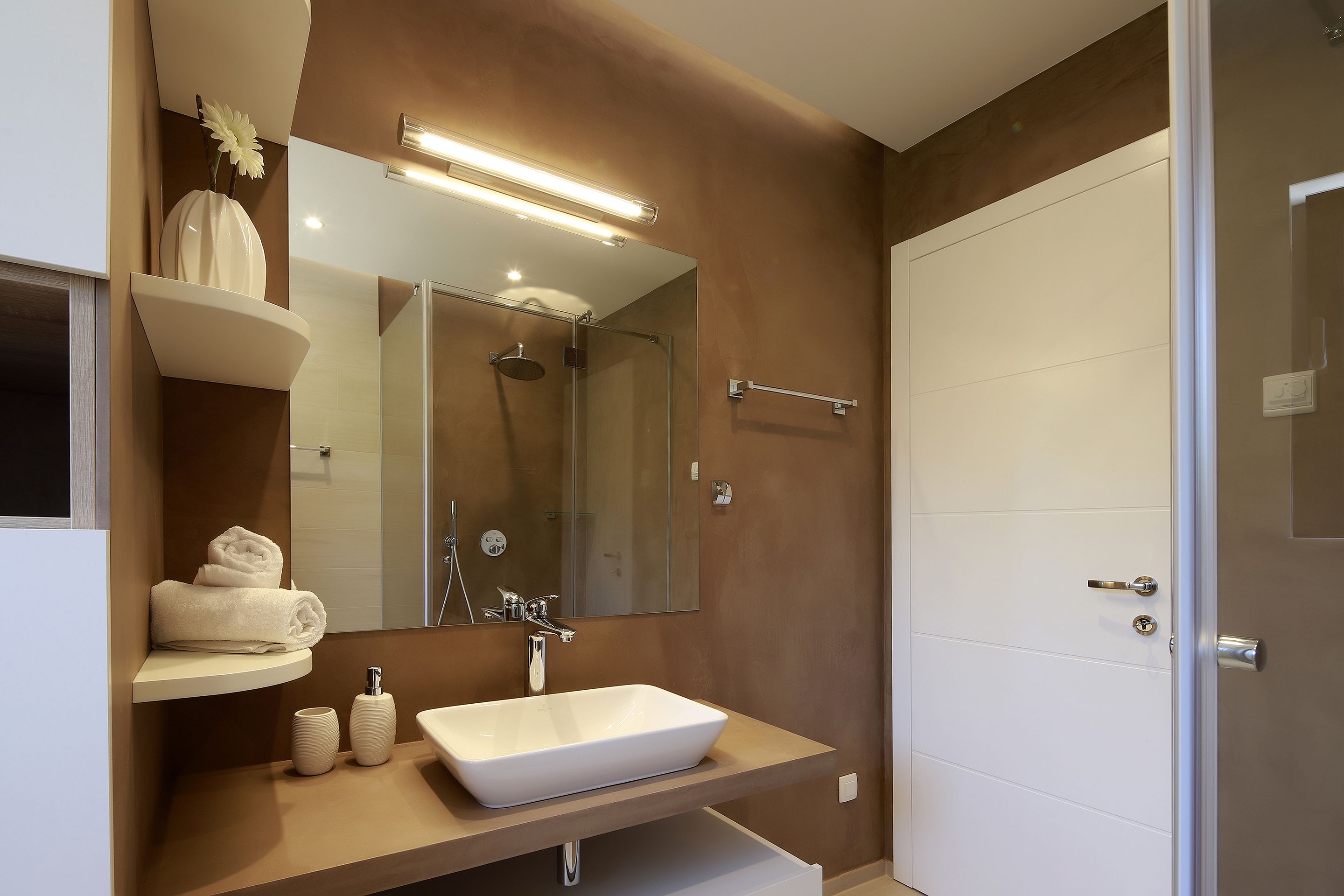 Un baño moderno con un espejo grande, un lavamanos blanco y una ducha.