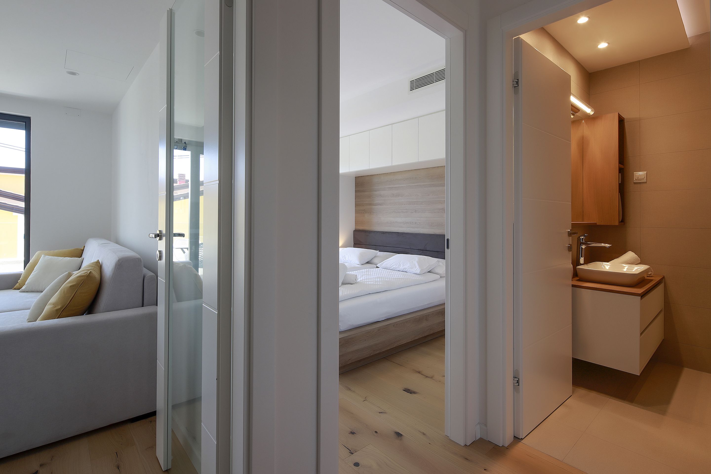 A modern bedroom with a bed, a sofa, and a bathroom with a sink and mirror.