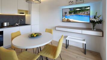 A modern kitchen with a built-in oven, a dining area with a round table and yellow chairs, and a TV mounted on the wall displaying a pool scene.