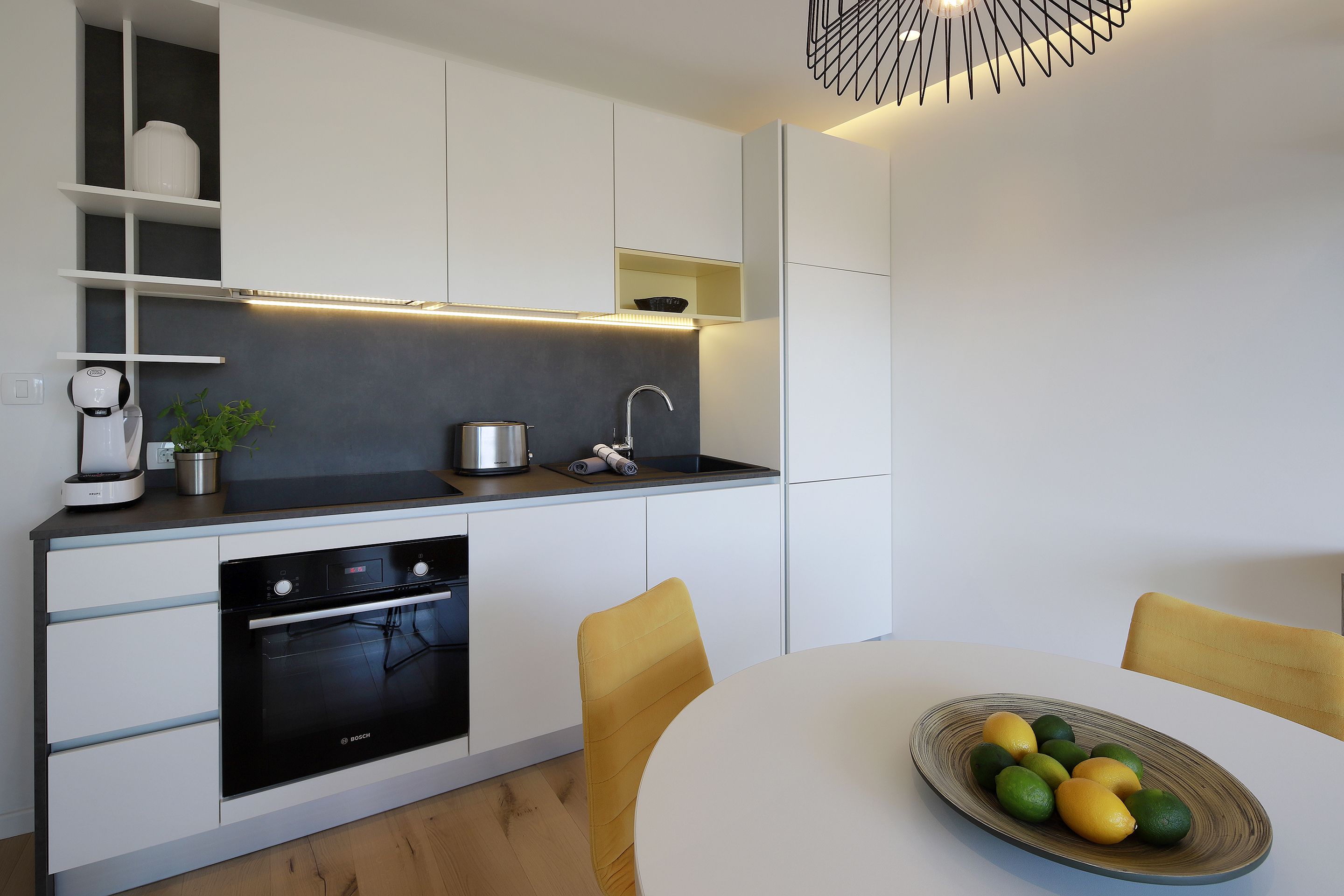 A modern kitchen with white cabinetry, a Bosch oven, and a dining table with chairs.