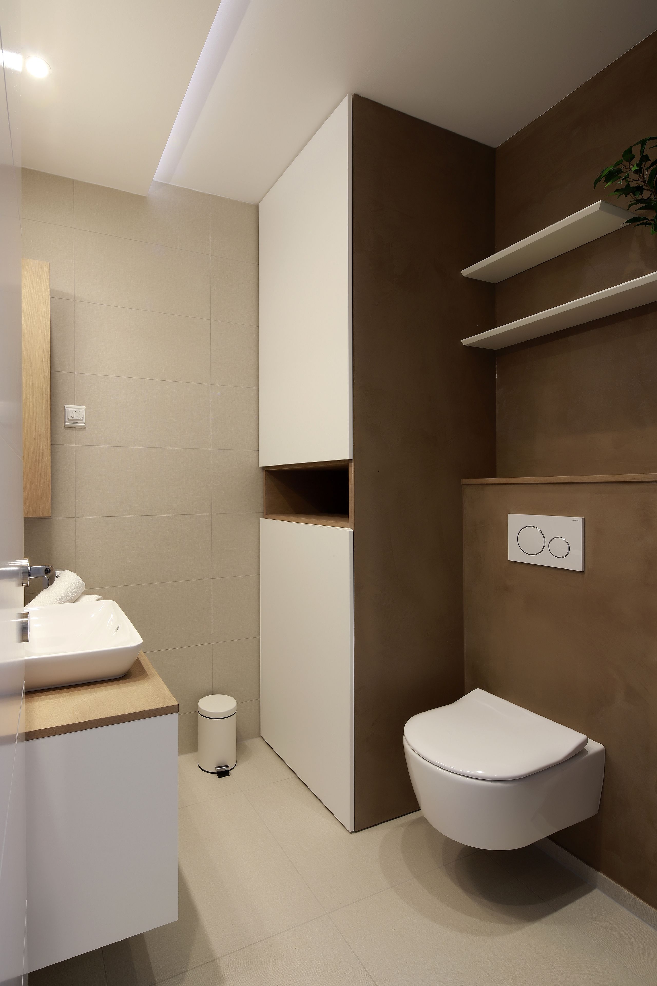 Un baño moderno con un lavabo blanco, un inodoro y estantes empotrados.