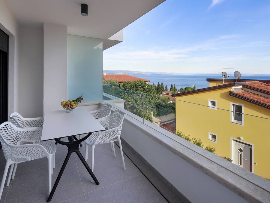A balcony with a white table and chairs, overlooking a cityscape and sea.