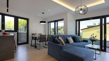 Een moderne woonkamer met een hoekbank, een eethoek en grote ramen.