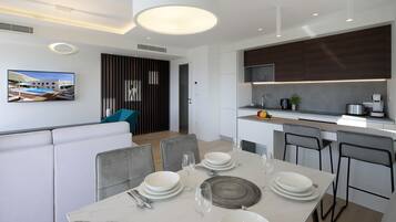 Un comedor moderno con una mesa de mármol dispuesta para cuatro personas, una cocina con armarios de madera oscura y un amplio ventanal con vistas a una piscina.