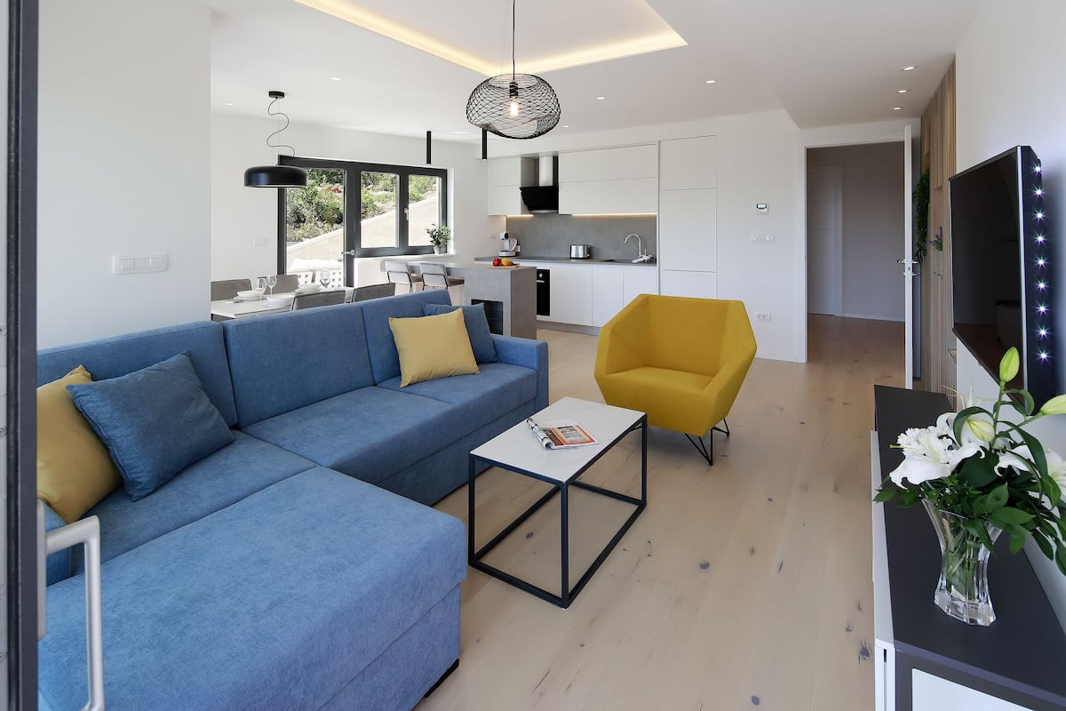A modern living room with a blue sectional sofa, a yellow armchair, and a coffee table.