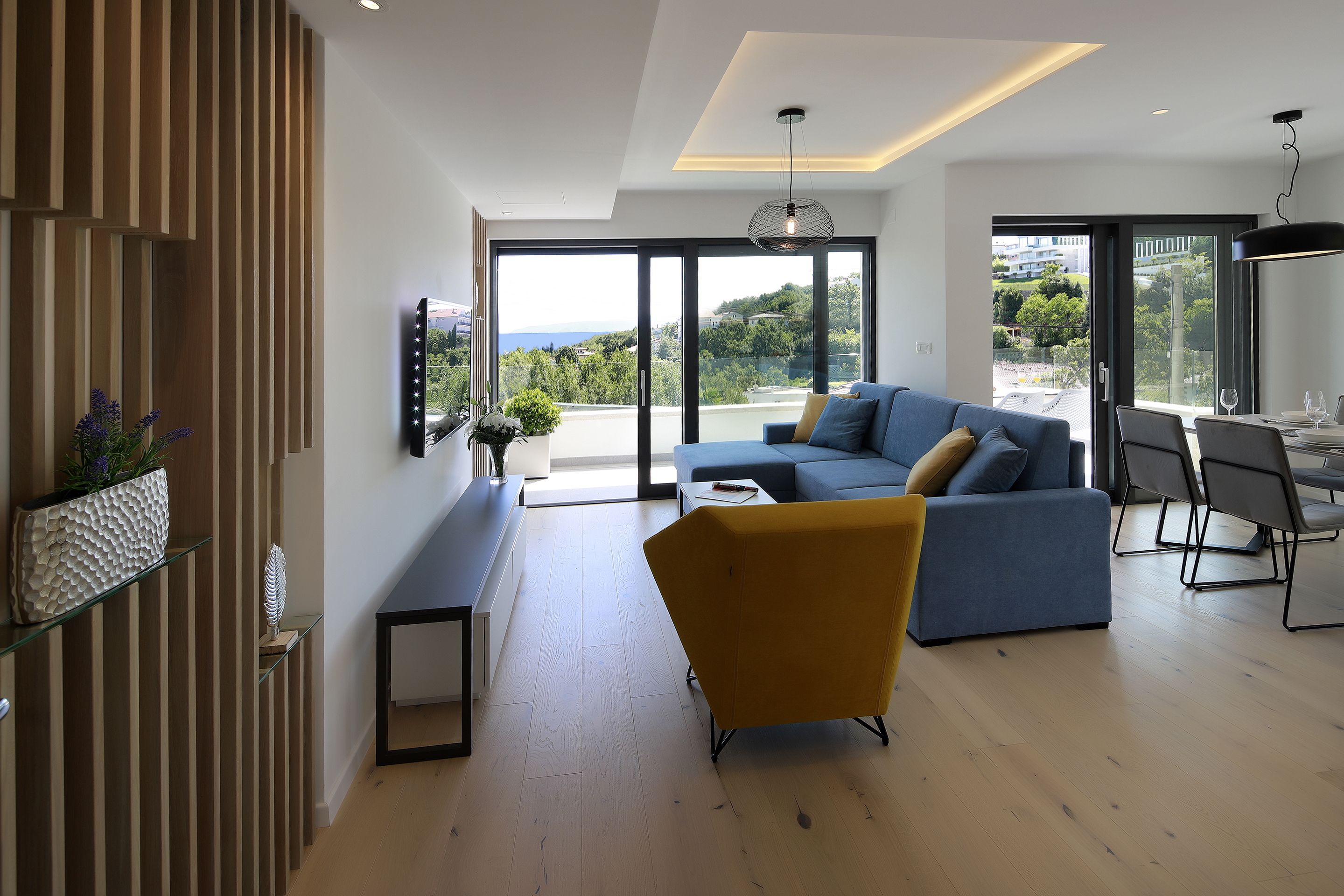 A modern living room with a sofa, a yellow armchair, and a dining area with a table and chairs.