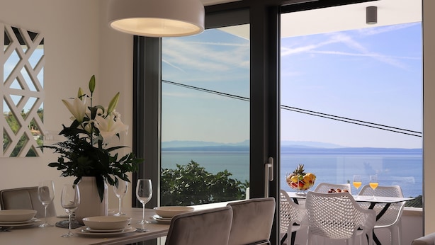 A dining area with a table set for two, a vase of flowers, and a view of the sea. - Modena Maris Apartments (Opatija)